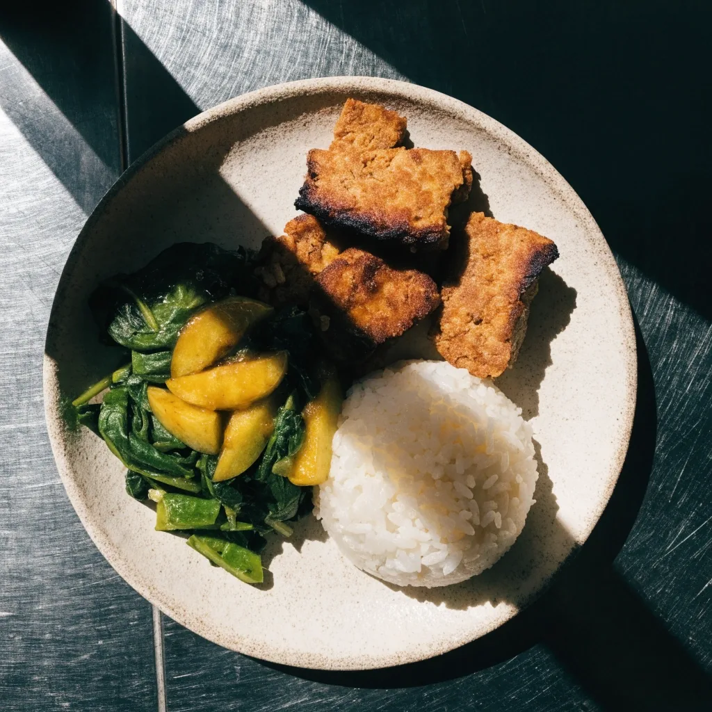 Piring makan siang dengan sayuran, lauk berprotein, dan nasi pada permukaan baja